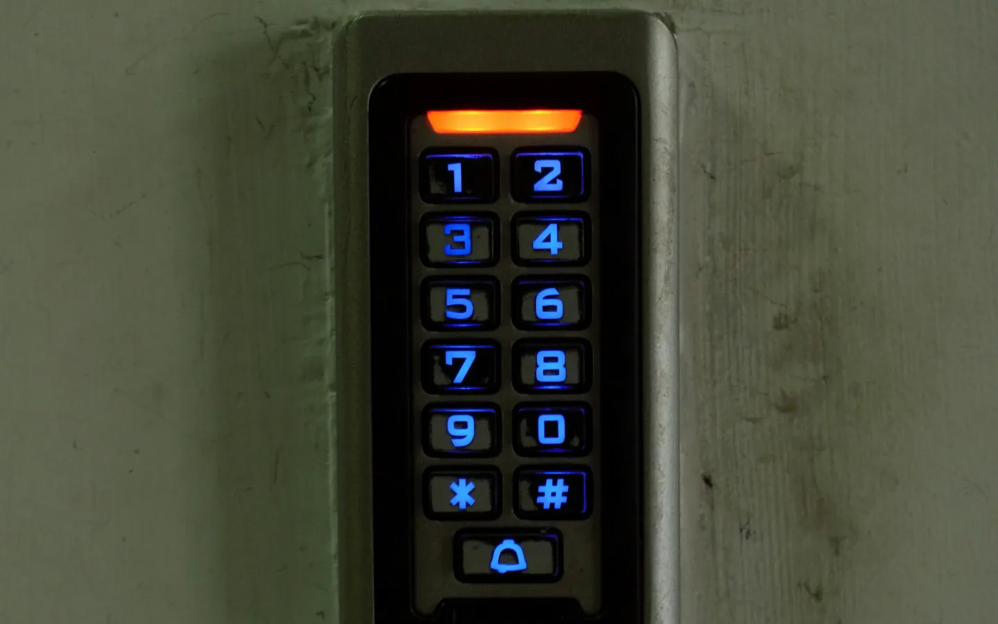An illuminated access-control keypad mounted on a concrete wall.